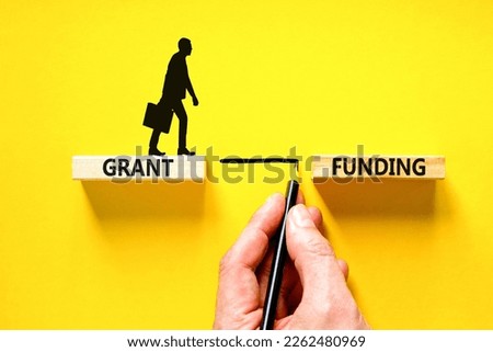 Grant funding symbol. Concept words Grant funding on wooden blocks. Beautiful yellow table yellow background. Businessman hand. Businessman icon. Business and grant funding concept. Copy space.