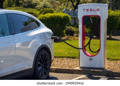 Grantham, UK - May 30th 2021: Tesla super charger plugged into a white tesla model x. In a motorway service area. High quality photo