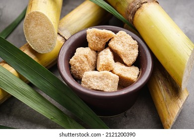 Granulated brown sugar, sugarcane and green leaf on a gray background, close-up.