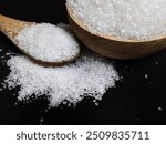 Granulated sugar filled in wooden bowl and spoon on black background. Close up view of white sugar