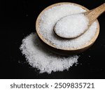 Granulated sugar filled in wooden bowl and spoon on black background. Close up view of white sugar