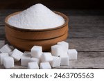 Granulated sugar in a wooden cup, a scattering of refined sugar cubes