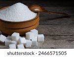 Granulated sugar in a wooden cup, a scattering of refined sugar cubes
