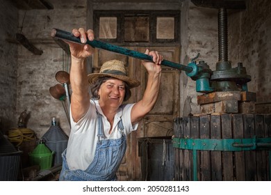 Récolte de raisins: Vieille femme viticole souriante travaillant sur une presse à vins traditionnelle pour le pressage du moût. Arrière-plan vieux vin