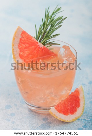 Grapefruit cocktail with ice and rosemary on blue background. Fresh raw grapefruit slices. Macro