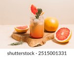 Grapefruit cocktail with rosemary garnish in a glass, served on a wooden cutting board. Vibrant, refreshing drink perfect for summer menu or cocktail recipes. Greyhound, lemonade, paloma, mocktail