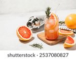 Grapefruit cocktail with rosemary garnish in a glass, served on a wooden cutting board. Vibrant, refreshing drink perfect for summer menu or cocktail recipes. Greyhound, lemonade, paloma, mocktail