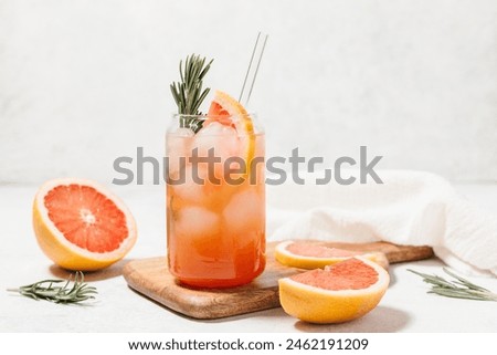Grapefruit cocktail with rosemary garnish in a glass, served on a wooden cutting board. Vibrant, refreshing drink perfect for summer menu or cocktail recipes. Greyhound, lemonade, paloma, mocktail