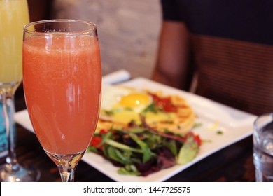 Grapefruit Mimosa with plate of brunch and person in background