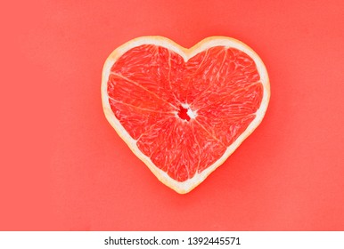 Grapefruit  In The Shape Of A Heart. The Concept Of Love For Vegetarian Food, Fruit Or Citrus Food. Сoral Color Grapefruit Background. Top View Or Flat Lay. Copy Space.