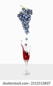 Grapes from bunch falling to transparent wineglass with red wine splash up, on white background