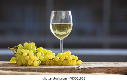 Grapes and white wine glass on a wooden table, black background, front view