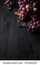 Grapevine on a wooden board. French vineyard. Wine bottle and cork. Dark wood background.