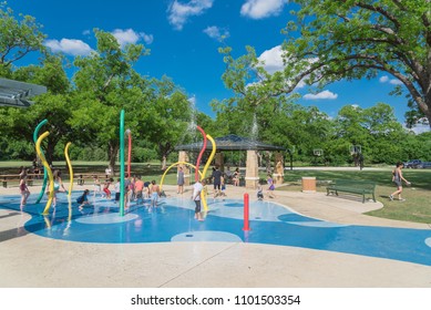 GRAPEVINE, TX, USA-May 28, 2018:Diverse Kids Enjoy Water Splash Pad Or Sprayground At Parr Park. Water Fountain Activities During Summer Time. Covered Pavilion, Trees Provide Shade For Parents