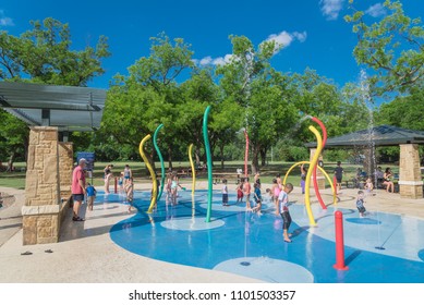 GRAPEVINE, TX, USA-May 28, 2018:Diverse Kids Enjoy Water Splash Pad Or Sprayground At Parr Park. Water Fountain Activities During Summer Time. Covered Pavilion, Trees Provide Shade For Parents