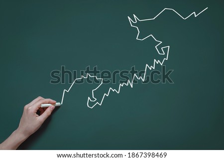 graph, diagram, chart of stock quotes drawn in chalk on a blackboard, the concept of trading, speculation, bulls and bears in the stock market, hand with chalk
