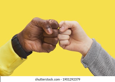 Graphic close up of two young people bumping fists against illuminating yellow background, interracial friendship and unity concept, copy space