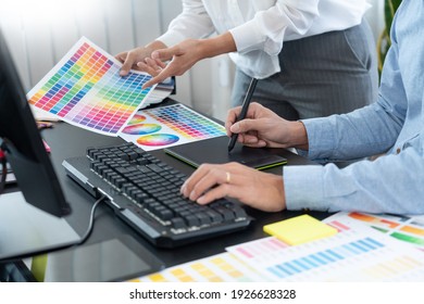 Graphic designer or creative working together coloring using graphics tablet and a stylus at desk with colleague