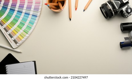 Graphic Designer Or Photographer Workspace With Colour Palette Samples, Stationery, Camera And Copy Space On White Background. Top View