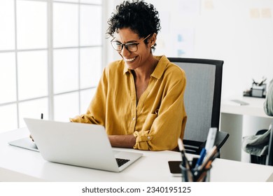 Graphic designer smiles as she works on a laptop in an office. Woman using a graphics tablet to make drawing designs. Creative business woman enjoys working on her project in an office. - Powered by Shutterstock