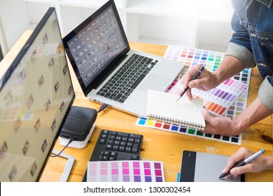 Graphic Designer Team Working On Web Design Using Color Swatches Editing Artwork Using Tablet And A Stylus At Desks In Busy Creative Office