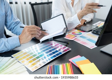 Graphic Designer Team Working On Web Design Using Color Swatches Editing Artwork Using Tablet And A Stylus At Desks In Creative Office.