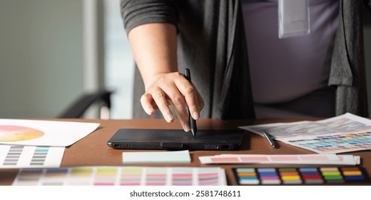 Graphic designer using a digital tablet to create designs at a wooden workspace.