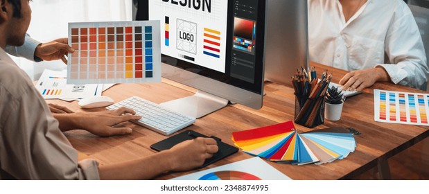 Graphic designer work on computer laptop and with graphic drawing pen while brainstorming unique design with professional graphic team in modern digital studio workplace. Panorama shot. Scrutinize