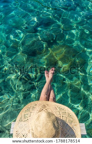 Graphic image of top down view of woman wearing big summer sun hat relaxing on small wooden pier by clear turquoise sea.