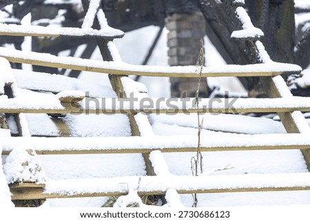 Graphic impression of burned down barn covered in snow after a blizzard snowstorm with the black wood and construction carcas contrasting against the white winter landscape