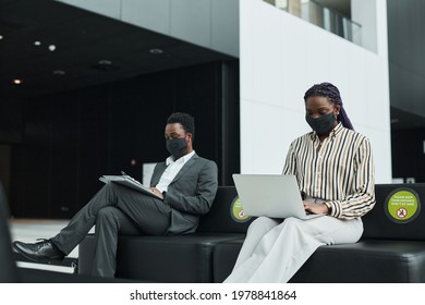 Graphic Portrait Of Two African-American Business People Wearing Masks While Working In Waiting Lounge At Airport With Social Distancing