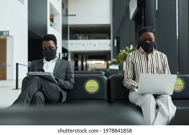 Graphic portrait of two business people wearing masks while working in waiting lounge at airport with social distancing