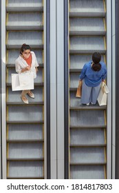 Graphic top down view at two women riding escalator in opposite directions while shopping in mall, focus on woman wearing mask looking up at camera, copy space
