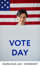 Graphic vertical shot of adult woman in voting booth with USA flag in background