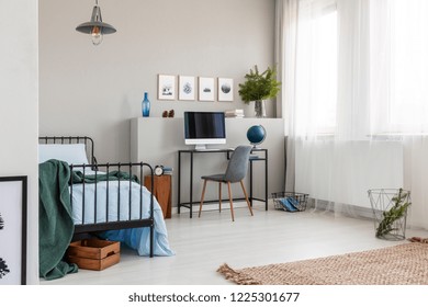 Graphics On The Empty Grey Wall Of Bright Teenager Bedroom With Single Metal Bed, Grey Chair And Industrial Desk With Globe And Computer