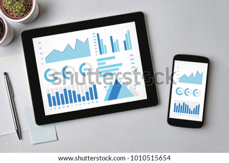 Graphs and charts elements on tablet and smartphone screen over gray table. All screen content is designed by me. Flat lay