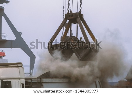 Grapple crane unloading cement clinker from ship to truck in river port. Barge delivery of dusty bulk cargo. Gantry crane unloading and loading in Harbor, outdoors. Logistics