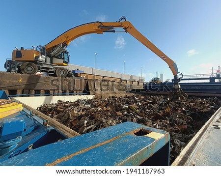 The grapple loading and unloading crane unloads metal and metal waste for recycling from the ship's hold. Ferrous scrap, non-ferrous scrap. Import and export of scrap for processing
