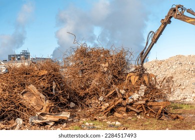 A grapple truck loads scrap industrial metal for recycling. Manipulator with a hydraulic magnetic crab against the sky. Crane garbage truck loading of industrial waste. - Powered by Shutterstock