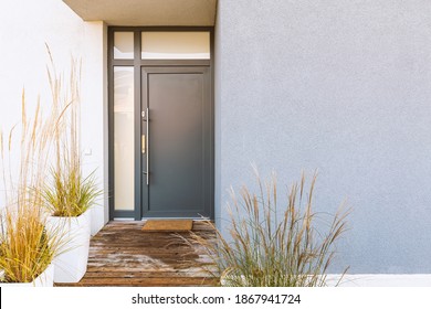 Hierba en la olla y camino de madera delante de la puerta delantera elegante casa suburbana