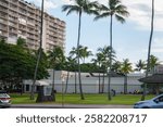 A grassy area with tall palm trees, a modern building, and the U.S. Army Museum of Hawaii sign. People walk and relax under sunny, clear skies.