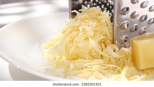grated cheese with a grater on a white plate. a piece of hard cheese next to shredded cheese close-up. parmesan cooking process. - Powered by Shutterstock