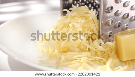 grated cheese with a grater on a white plate. a piece of hard cheese next to shredded cheese close-up. parmesan cooking process.
