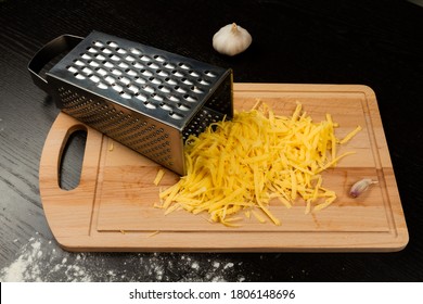 grated fresh aromatic cheese for pizza, garlic and grater lie on a wooden kitchen board