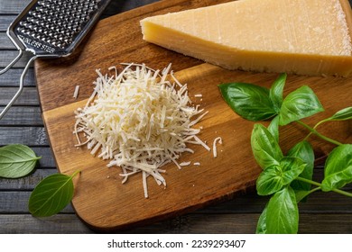 Grated parmesan cheese on a cutting board. Italian grana padano cheese whole and grated, grater and fresh basil herb over wooden background. Delicious hard cheese, dairy product. Top view. - Powered by Shutterstock