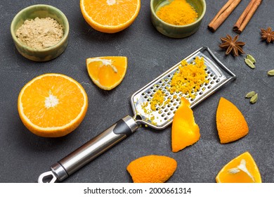 Grated Zest On Grater. Slice Of Orange Peel On Grater. Orange Halves, Dry Ginger And Turmeric, Spices On Table. Black Background. Top View
