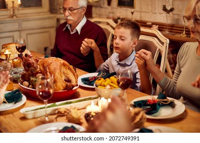 Grateful Extended Family Saying Grace During Thanksgiving Dinner At Dining Table. Focus Is On Small Boy.