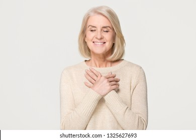 Grateful Happy Mature Old Woman Holding Hands On Chest Feeling Hopeful Thanking For Honesty Love Sincere Appreciation, Touched Pleased Middle Aged Senior Lady Isolated On White Grey Studio Background