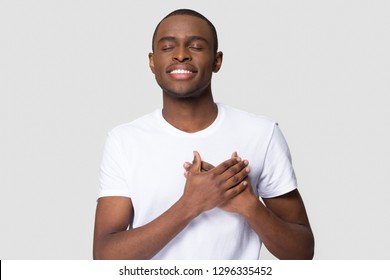 Grateful happy pleased african man holding hands on chest to heart feeling love appreciation gratitude honesty, thankful sincere proud black guy thanking isolated on white studio blank background