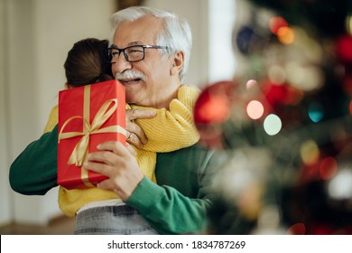 Grateful little girl embracing her grandfather while receiving Christmas present at home. Focus is on man.  - Powered by Shutterstock